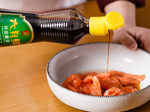 將三文魚(yú)薄片，用六月鮮特級醬油、料酒和胡椒粉腌漬 5 分鐘。